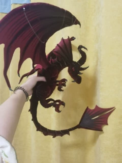 Black and purple handmade pipe cleaner dragon posed against a yellow wall, buyer photo